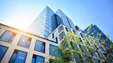 Ofis binasının alt manzarası gün doğumu, yansıma ve perspektifle kapanıyor. Güneş ışınlı modern mimari. Parlak güneşli bir günde, masmavi gökyüzünde güneş ışınlarıyla cam cephe. 