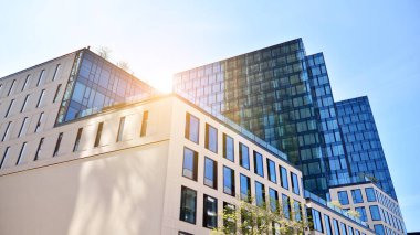 Ofis binasının alt manzarası gün doğumu, yansıma ve perspektifle kapanıyor. Güneş ışınlı modern mimari. Parlak güneşli bir günde, masmavi gökyüzünde güneş ışınlarıyla cam cephe. 