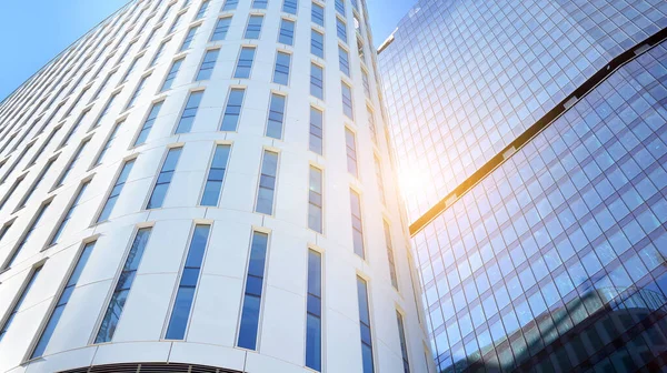 Ofis binasının alt manzarası gün doğumu, yansıma ve perspektifle kapanıyor. Güneş ışınlı modern mimari. Parlak güneşli bir günde, masmavi gökyüzünde güneş ışınlarıyla cam cephe. 