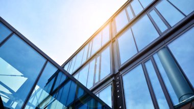 Ofis binasının alt manzarası gün doğumu, yansıma ve perspektifle kapanıyor. Güneş ışınlı modern mimari. Parlak güneşli bir günde, masmavi gökyüzünde güneş ışınlarıyla cam cephe. 