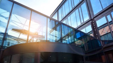 Ofis binasının alt manzarası gün doğumu, yansıma ve perspektifle kapanıyor. Güneş ışınlı modern mimari. Parlak güneşli bir günde, masmavi gökyüzünde güneş ışınlarıyla cam cephe. 