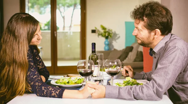 Hombre y mujer enamorados tomados de la mano mirando a los ojos a la mesa en casa —  Fotos de Stock