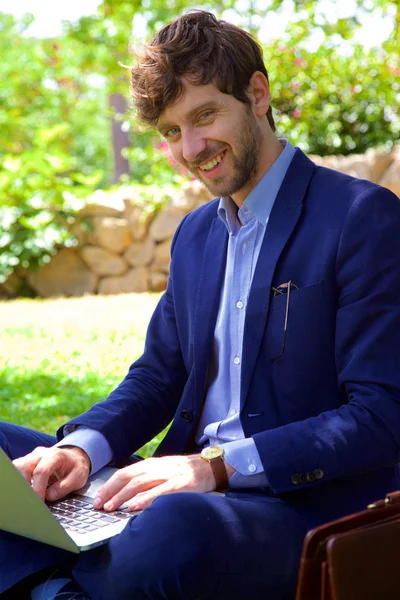 Hombre guapo trabajando en primavera en el parque con el portátil sonriendo mirando cámara —  Fotos de Stock