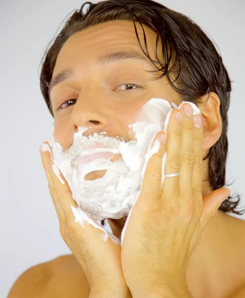 Feliz hombre sonriente aplicando crema en la cara antes de afeitarse mirando cámara — Foto de Stock