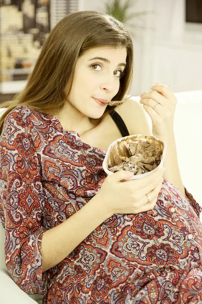 Linda mujer embarazada sonriente comiendo helado de chocolate en casa mirando cámara —  Fotos de Stock