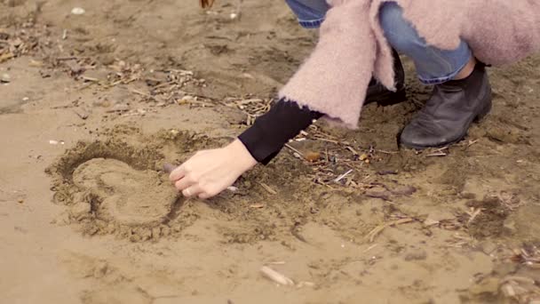 Женщина одна на пляже думает о любви рисует сердце на песке — стоковое видео