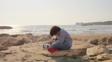 Sahilde cep telefonuyla oynayan mutlu çocuk.