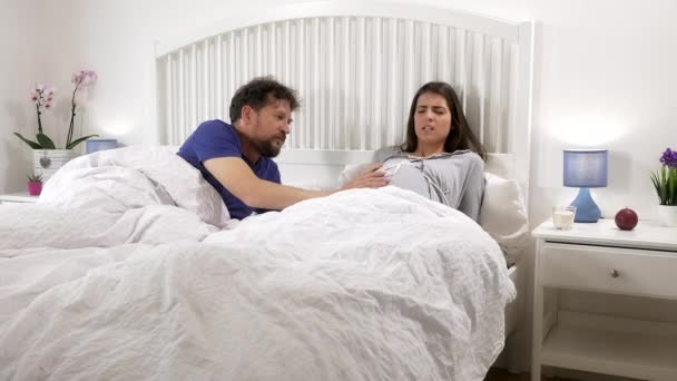 Pregnant woman with contractions in bed worried husband talking to her medium shot — Stock Video