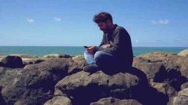 Okyanusun önünde tatilde olan bir adam cep telefonuyla gülümsüyor.