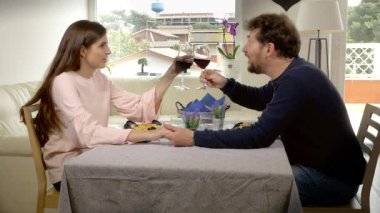 Evde aşık mutlu çift romantik öğle yemeğinde şarapla kadeh kaldırıyor.