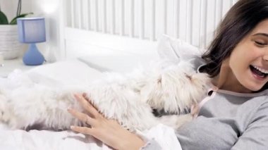 Köpek yatakta kadını yalıyor. Yüzünde komik bir ifade var.