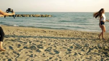 Gün batımında sahilde dans eden kızlarla video klip sahnesinin arkasında.