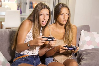 Cute girls playing with video games at home having fun clipart