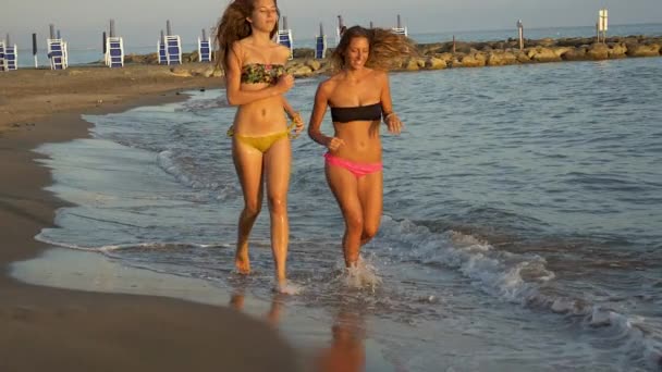 Süße junge Frauen joggen im Meer am Strand glücklich lächelnd in Zeitlupe — Stockvideo