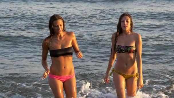 Meninas bonitas saindo do mar ao pôr do sol câmera lenta tiro médio — Vídeo de Stock