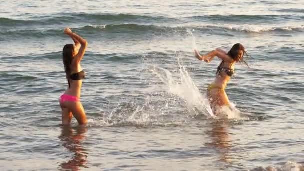 Chicas felices salpicando en el océano divirtiéndose al atardecer super cámara lenta — Vídeo de stock
