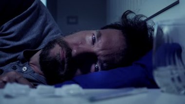 Geceleri üzgün, yalnız bir adam. Yatakta uzanmış kameraya bakıyor.