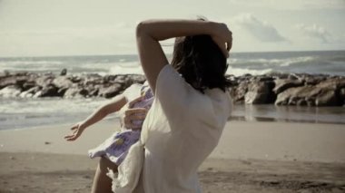 Aşk ve mutluluk kavramı, gün batımında küçük kızını sahilde kucağına alan anne, yavaş çekim, film görüntüsü.