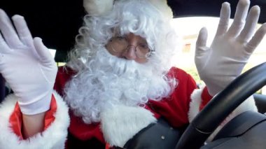 Noel Baba arabada merhaba diyor ve kameraya bakıyor, ağır çekim.