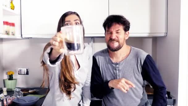 Смешные мужчина и женщина в пижаме на кухне смотрят в камеру и пьют кофе, танцуя. — стоковое видео