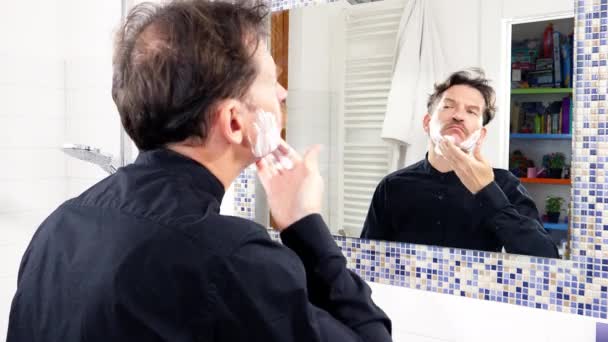 Elegante bell'uomo che mette la crema da barba sul viso davanti allo specchio a casa — Video Stock