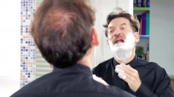 Смешное выражение элегантного мужчины, пачкающего рубашку при нанесении крема для бритья — стоковое видео