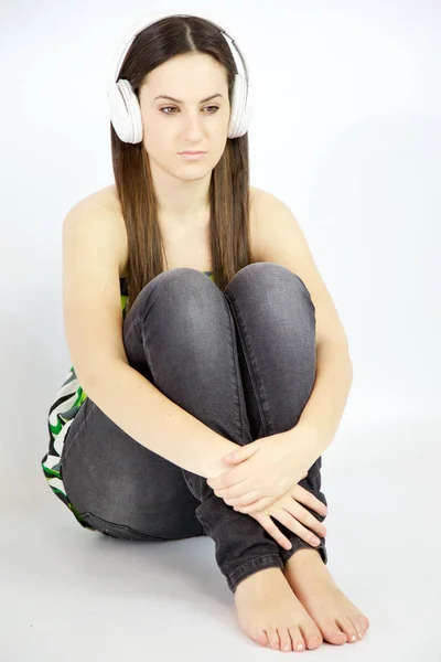 Smutná žena poslech hudby se sluchátky na uších sedí na podlaze myšlení — Stock fotografie