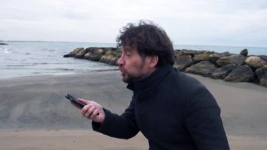 İş adamı kışın okyanusun önünde telefonda bağırıyor, ağır çekimde, orta çekimde.