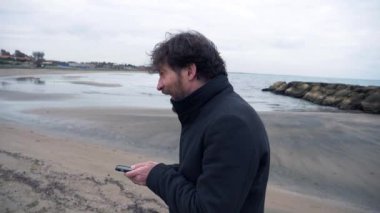 İş adamı kışın ağır çekimde okyanusun önünde telefonda bağırıyor.