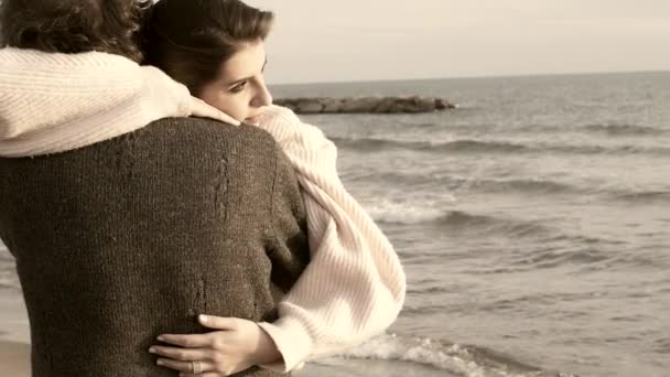 彩度の低い秋のスローモーション ミディアム ショットのビーチに夕日を見て彼氏を抱いて愛の女 — ストック動画