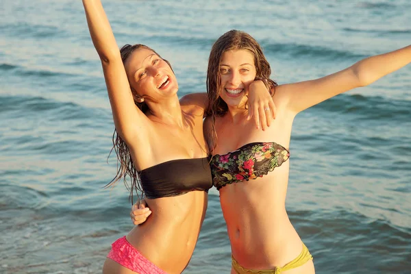 Meninas bonitas molhadas sorrindo em biquíni no oceano ao pôr do sol — Fotografia de Stock