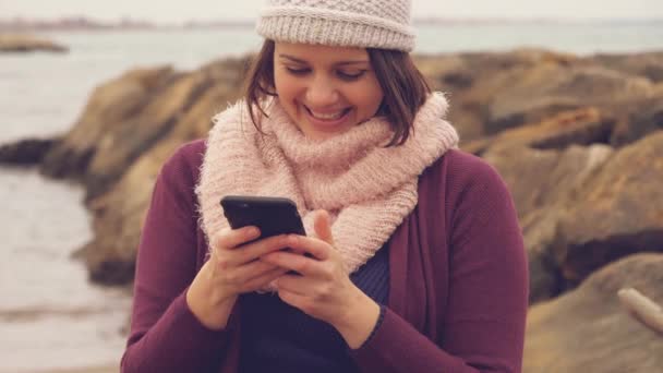 幸せな日没のスローモーションが笑顔で海の前電話で女性テキスト メッセージ — ストック動画