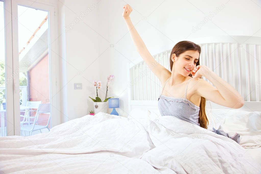 Cute happy woman in hotel in the morning stretching waking up