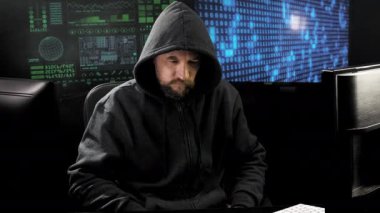 Kapüşonlu adam stüdyoda ekranın önünde hoparlörden konuşuyor.