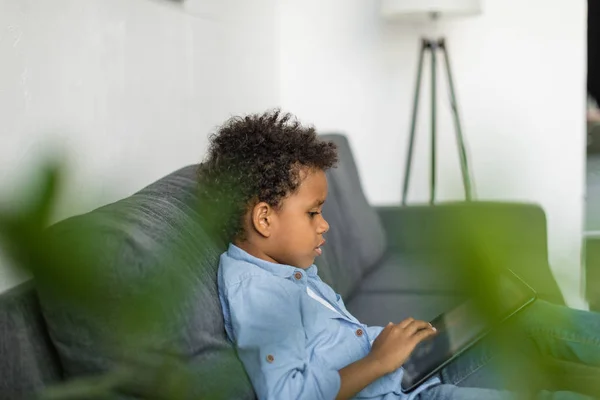 Niño reflexivo utilizando la tableta digital en el sofá — Foto de Stock