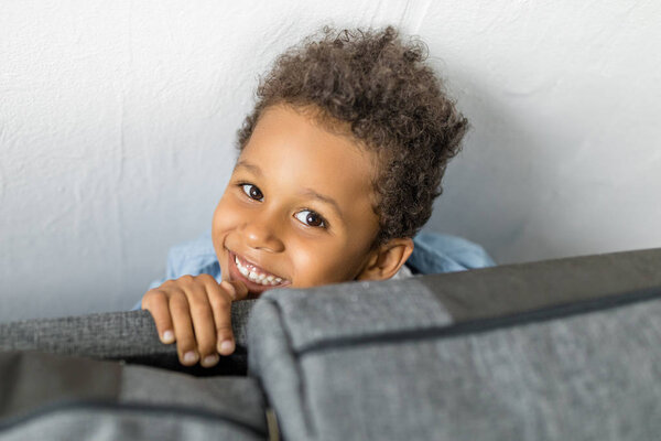 adorable afro boy hiding by sofa