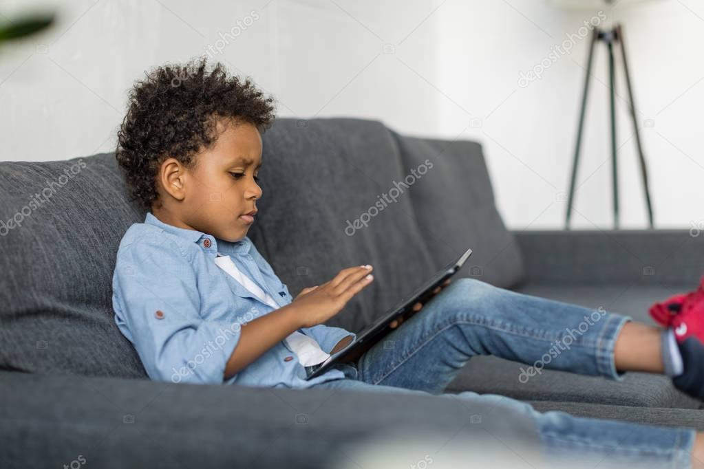 thoughtful boy using digital tablet on sofa