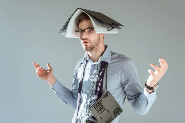 年轻糊涂商人持有笔记本电脑在他的头上 电话在脖子上孤立的灰色 — 图库照片
