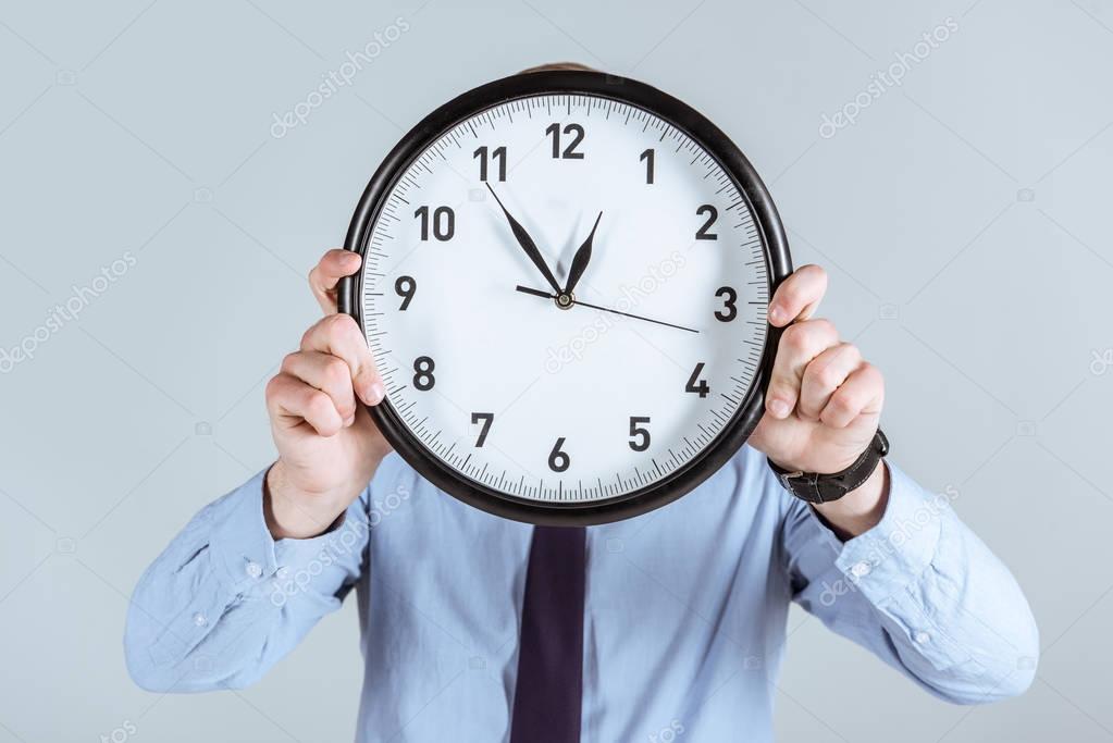 Businessman in shirt holding clock over his face isolated on grey 