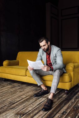 gazete okuma ve sarı koltukta oturan takım elbiseli şık adam 