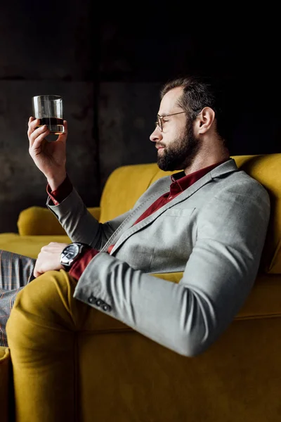 bearded handsome man looking at glass of whiskey