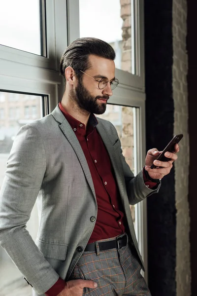 Κομψό Όμορφος Άνδρας Στην Επίσημη Ένδυση Χρησιμοποιώντας Smartphone Στο Παράθυρο — Φωτογραφία Αρχείου