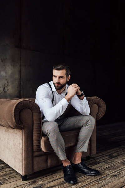 Модный красивый задумчивый мужчина сидит в кресле на чердаке
