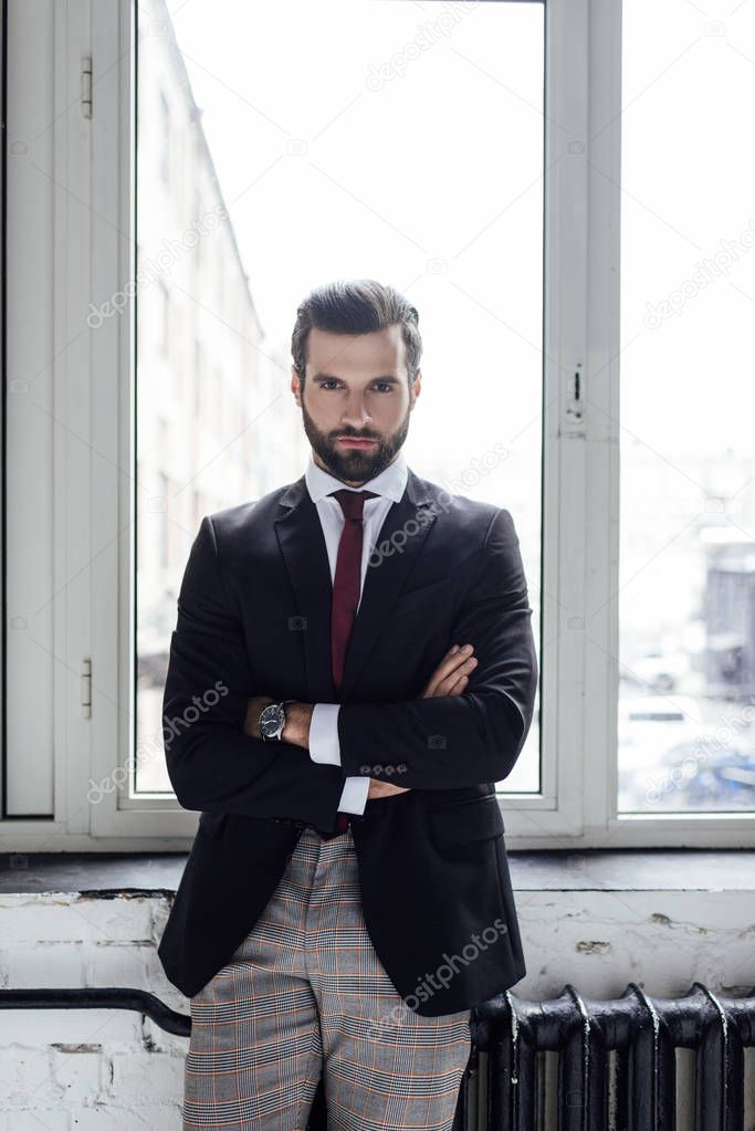 handsome serious businessman posing with crossed arms at window