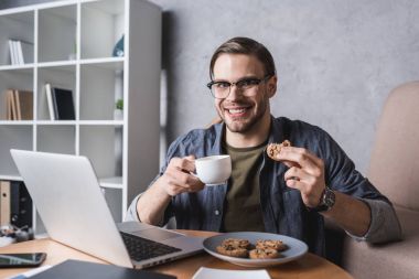 laptop ile çalışma ve çerezleri yiyip kahve yakışıklı delikanlı