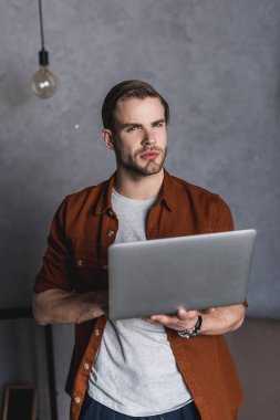 laptop ile çalışma ve kameraya bakarak genç thiughtful adam