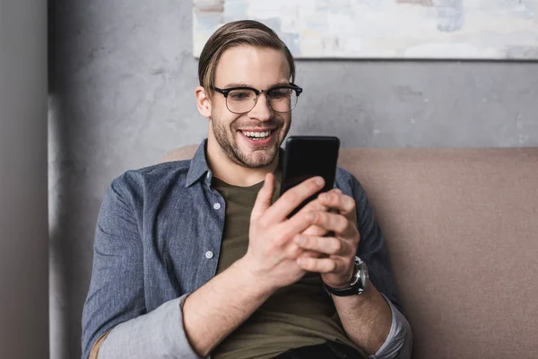 Jovem Feliz Usando Smartphone Enquanto Sentado Sofá — Fotografia de Stock