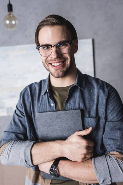 smiling young man in eyeglasses holding book