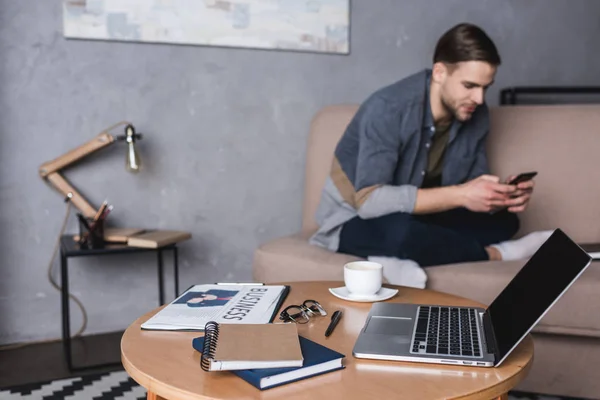 Jovem Homem Bonito Usando Smartphone Sofá Com Laptop Suprimentos Negócios — Fotografia de Stock