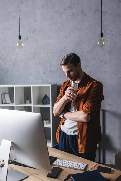 Nachdenklicher Junger Geschäftsmann Trinkt Wasser Und Schaut Auf Den Computer — Stockfoto